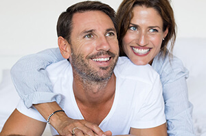 Smiling couple embracing on a white bed.